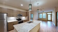 Located at 900 Grange Hall Dr in Euless, TX, this well-appointed 2-bedroom, 2-bathroom residence offers a thoughtfully designed single-floor layout. The open-concept kitchen serves as the heart of the home, showcasing a large granite-topped island with an undermount sink, sleek wood-grain cabinetry, a white subway tile backsplash, and a full suite of stainless steel appliances including a refrigerator, range, and over-the-range microwave. Stylish pendant lighting adds a modern touch above the island. The kitchen flows seamlessly into the living room, which features warm wood-style plank flooring, a ceiling fan, and windows with exterior access that bring in generous natural light. Both bedrooms are carpeted and include ceiling fans, windows overlooking the outdoors, and dedicated closets with built-in shelving systems for organized storage. The bathrooms are finished with large-format tile flooring, wood-toned vanities, granite countertops, and wide framed mirrors. A connecting hallway ties the bedrooms and bathrooms together efficiently. Throughout the residence, neutral tones and contemporary finishes create a clean, cohesive aesthetic that is both functional and inviting.