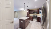 Located at 910 Patriot Dr in Mankato, MN, this 1-bedroom, 1-bathroom unit with a den offers a well-designed, single-level layout. The open-concept kitchen is a standout feature, showcasing rich dark wood cabinetry, granite countertops, a large center island with pendant lighting overhead, and a full suite of stainless steel appliances including a refrigerator with ice maker, electric range, and built-in microwave. Tile flooring runs throughout the kitchen and extends into the entryway, while plush wall-to-wall carpeting covers the living areas, bedroom, and den. The spacious living room is filled with natural light from a large sliding glass door that opens to a private balcony, offering outdoor views of the surrounding area. The bedroom includes a ceiling fan, a generously sized window, and dedicated closet space. The den provides a versatile additional room suited for a home office or guest space. The full bathroom features a dark wood vanity with a white countertop, tile flooring, and a large mirror. Additional conveniences include in-unit laundry, a utility room, and ample closet storage throughout the unit.