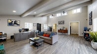 Located at 1810 Monterey Rd in Colorado Springs, CO, this single-floor space makes a strong architectural impression despite its compact footprint. The most defining feature is the dramatic vaulted ceiling adorned with exposed structural beams, which creates a sense of vertical openness that far exceeds what the floor area alone might suggest. Dual ceiling fans are mounted at height, and clerestory windows positioned near the roofline invite abundant natural light throughout the day, complementing the larger windows along the walls.

The living area serves as the central hub of the space, finished with wide-plank, wood-look luxury vinyl flooring in a cool gray tone that runs consistently throughout. A sleek wall-mounted electric fireplace anchors one end of the room, while a reception-style desk area near the entrance suggests versatile functionality. Neutral gray walls provide a clean, modern backdrop.

The kitchen is accessible from the main living area and continues the cohesive design aesthetic. The bathroom features granite-look countertops, dark cabinetry, and matching wood-look flooring, maintaining a polished and consistent style. A dedicated hallway leads to a clean, simply appointed restroom. Overall, the space presents a modern, open, and efficiently designed interior with notable architectural character.