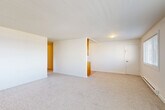 Located at 480 S State St in Bellingham, Washington, this two-bedroom, one-bathroom residence offers a practical and well-organized single-floor layout. The open combined living and dining area is anchored by neutral carpet flooring, crisp white walls, and a pass-through connection to the kitchen, creating a bright and cohesive common space. The galley-style kitchen is outfitted with warm wood cabinetry, granite-look countertops, a double-basin stainless steel sink, and light hardwood-style flooring, providing ample storage and counter space for everyday use. Both bedrooms feature plush carpet, natural light from exterior-facing windows with outdoor views of the surrounding neighborhood, and baseboard heating. Sliding closet doors in the bedrooms offer convenient storage, complemented by a total of four closets throughout the unit. The full bathroom includes a tub and shower combination with classic blue tile surround and chrome fixtures. A central hallway connects the living spaces to the bedrooms and bathroom, and conveniently houses a stacked in-unit washer and dryer. The layout is efficient and functional, making excellent use of the available space throughout.