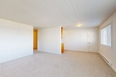 Located at 480 S State St in Bellingham, Washington, this two-bedroom, one-bathroom residence offers a practical and well-organized single-floor layout. The open combined living and dining area is anchored by neutral carpet flooring, crisp white walls, and a pass-through connection to the kitchen, creating a bright and cohesive common space. The galley-style kitchen is outfitted with warm wood cabinetry, granite-look countertops, a double-basin stainless steel sink, and light hardwood-style flooring, providing ample storage and counter space for everyday use. Both bedrooms feature plush carpet, natural light from exterior-facing windows with outdoor views of the surrounding neighborhood, and baseboard heating. Sliding closet doors in the bedrooms offer convenient storage, complemented by a total of four closets throughout the unit. The full bathroom includes a tub and shower combination with classic blue tile surround and chrome fixtures. A central hallway connects the living spaces to the bedrooms and bathroom, and conveniently houses a stacked in-unit washer and dryer. The layout is efficient and functional, making excellent use of the available space throughout.