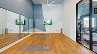 This state-of-the-art fitness facility, located at 2735 McGinnis Ferry Rd in Suwanee, GA, boasts an impressive 1,840 square feet of exercise space. The center features a striking architectural design with vaulted ceilings adorned with modern, star-shaped light fixtures that create a sense of openness and energy. Large windows line the walls, flooding the space with natural light and offering views of the surrounding area.

The gym is divided into distinct zones to accommodate various workout styles. The cardio area is equipped with top-of-the-line treadmills and stationary bikes, each facing mounted televisions for entertainment during workouts. The strength training section includes a comprehensive selection of weight machines and free weights, catering to all levels of fitness enthusiasts.

A dedicated area for functional training and stretching features battle ropes, stability balls, and open floor space. The facility also incorporates a serene yoga studio with hardwood flooring, full-length mirrors, and calming wall art, perfect for mindfulness practices.

The interior design utilizes a cool, calming color palette of grays and blues, creating a motivating yet relaxing atmosphere. The herringbone-patterned carpeting throughout most of the space adds a touch of sophistication while providing necessary cushioning for exercise activities.

Overall, this fitness center combines functionality with aesthetic appeal, offering a premium workout experience in a thoughtfully designed environment.