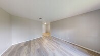 This single-floor, one-bedroom, one-bathroom unit offers a practical and well-organized layout across a compact yet functional footprint. Consistent light-toned hardwood-style flooring runs throughout, lending a clean, cohesive aesthetic to the entire space.

The living area is open and airy, featuring neutral gray walls, white baseboards, and a window that invites natural light while offering views of an outdoor greenery. A front entry door is positioned conveniently adjacent to the window, making the entry welcoming and bright.

The kitchen is designed in a galley-style configuration, maximizing efficiency in a narrow space. White shaker cabinetry with matte black hardware lines both sides, complemented by light speckled countertops, a stainless steel sink, a stainless steel refrigerator, and a stainless steel range with an electric cooktop. A tray ceiling detail adds architectural character overhead.

The bedroom is a comfortable, well-proportioned space outfitted with a ceiling fan with light fixture and a window offering outdoor views. A hallway from the bedroom leads directly to the bathroom, providing added privacy. A dedicated closet is also accessible from this corridor.

The bathroom features a full tub-shower combination with a white surround and matte black fixtures, paired with a dark-toned vanity with a sink, offering a modern contrast against the neutral walls.