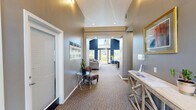 Located in Beaverton, Oregon, this single-floor community amenity space offers a thoughtfully designed layout that blends comfort and functionality. The interior is defined by soaring vaulted ceilings and a bold two-tone color palette of deep navy blue and warm gray, creating a striking yet inviting atmosphere throughout.

The living room serves as a central gathering space, anchored by a tile-surround fireplace with a classic white mantle and a wall-mounted television above. Plush gray seating, carpeted floors, and multiple windows dressed with white blinds fill the room with natural light and outdoor views of the surrounding greenery.

Adjacent to the living area, the dining room features a large oval wooden table with seating for several guests, bathed in natural light from a generous bank of windows. A built-in kitchenette with white cabinetry, a sink, and small appliances adds convenience for gatherings and events.

The exercise room is well-equipped with a variety of cardio and strength-training machines, including treadmills, a cable machine, a recumbent bike, and a stair climber. Rubber flooring, a wall-mounted television, and large windows provide a comfortable and motivating workout environment. Connecting hallways link each area seamlessly, completing this versatile and functional community space.