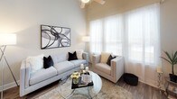 This single-story residence showcases a thoughtfully designed open-concept layout with a neutral color palette and contemporary finishes throughout. The living area is a standout space, distinguished by soaring ceilings and an abundance of natural light streaming through floor-to-ceiling windows dressed with sheer curtains. Wood-look plank flooring anchors the space, and a ceiling fan adds both style and practicality. A sliding glass door leads to a private patio, further enhancing the sense of openness.

The kitchen is well-appointed with warm-toned wood cabinetry extending to the ceiling, a tiled backsplash, granite countertops, and a full suite of stainless steel appliances. A central island with seating for two serves as both a dining and entertaining hub, illuminated by elegant pendant lighting.

The bedrooms feature plush carpeting, ceiling fans, and windows that allow ample natural light. One bedroom includes a dark-finished dresser with a round mirror, adding a modern touch. The bathroom is finished with matching wood cabinetry, granite countertops, a wide vanity mirror, and wood-look flooring, creating a cohesive and polished aesthetic throughout the home.