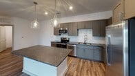 Located in Grandover Village in Greensboro, NC, this single-floor residence offers a thoughtfully designed layout with modern finishes throughout. The kitchen serves as a functional centerpiece, featuring gray shaker-style cabinetry, dark granite countertops, a white subway tile backsplash, and a full suite of stainless steel appliances, including a refrigerator with ice maker, electric range, microwave, and dishwasher. A kitchen island provides additional prep space, while pendant globe lighting adds a contemporary touch above. Wood-look flooring runs throughout the main living and kitchen areas, contributing to a cohesive, modern aesthetic.

The bedrooms are carpeted for comfort and each includes a ceiling fan with light fixture and a window with blinds, allowing for natural light and outdoor views. The bathrooms are finished with dark wood vanities, light granite countertops, large mirrors, and stone-look tile flooring. One bathroom features a tub-shower combination, while another offers a walk-in shower. A dedicated laundry room houses a full-size GE washer and dryer with wire shelving above, adding practical convenience. The overall interior presents a clean, neutral palette with consistent, updated finishes throughout.