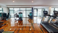 This fitness center is a thoughtfully designed, single-floor facility that combines functionality with an appealing aesthetic. The standout feature underfoot is the eye-catching, high-gloss hardwood floor inlaid with a geometric pattern of contrasting dark green and natural wood tones, lending the space a dynamic and polished character.

The facility is divided into clearly defined workout zones. A dedicated cardio area lines the perimeter and features a row of Matrix treadmills, elliptical trainers, and stationary bikes. Floor-to-ceiling windows and glass panel walls along the exterior wall flood the space with natural light and offer open views of the surrounding greenery, creating an energizing workout environment.

The strength training zone is outfitted with Matrix cable and functional training machines, adjustable benches, and a multi-use rack system. A dedicated free weights corner provides a full dumbbell rack alongside a green rubber flooring mat for safety and comfort. Large wall-mounted mirrors expand the visual scale of the space and allow users to monitor their form.

Recessed lighting throughout ensures consistent illumination, while wall-mounted flat-screen televisions keep members entertained during workouts. A wall-mounted fan and climate control units support a comfortable environment year-round. The space is accessed through sleek double glass doors, completing the clean and modern design of this comprehensive fitness facility.