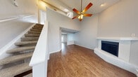 Located at 1800 Southseas Ln in Arlington, TX, this two-story home offers a well-defined layout with distinct living spaces across both levels. The main living area immediately commands attention with its dramatic vaulted ceilings, accented by a skylight and a ceiling fan that enhances airflow throughout the open space. Rich wood-look flooring runs throughout the main level, complementing the neutral gray walls and creating a warm, cohesive aesthetic. A white-mantled fireplace serves as a focal point, adding character to the living room, which flows openly into an adjacent area with views toward the front windows. The kitchen is equipped with dark espresso cabinetry, a white subway tile backsplash, gray countertops, a double-basin sink, and stainless steel appliances including a refrigerator, range, and built-in microwave. A bathroom on the main level includes a tub/shower combination with a window providing natural light. Upstairs, the bedrooms feature vaulted ceilings, plush neutral carpeting, ceiling fans, and large windows that invite natural light and outdoor views. The overall ambiance of the home is clean, bright, and functional, with an architectural design that emphasizes vertical space and an open feel throughout.