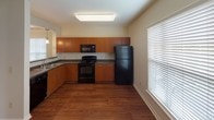 Located at 10617 Eddings Dr in Charlotte, NC, this single-floor residence offers a thoughtfully arranged layout designed for comfortable everyday living. The kitchen is a functional highlight, featuring warm medium-toned wood cabinetry, dark granite-style countertops, and a full suite of black appliances including a range, over-the-range microwave, and refrigerator. Rich hardwood-style flooring anchors the kitchen and extends into the bathroom areas, adding warmth and continuity throughout. A pass-through opening connects the kitchen to the dining and living areas, promoting an open, connected feel. The living and dining spaces are generously proportioned, with neutral carpet, crown molding, and large windows fitted with blinds that allow ample natural light while maintaining privacy. The bedrooms are carpeted and feature neutral tones, with windows overlooking the outdoors and access to closet space, including a walk-in closet with built-in shelving. The bathrooms are finished with hardwood-style flooring, a white vanity with integrated sink, and a tiled tub-shower combination. The overall aesthetic throughout the home is clean and neutral, providing a versatile canvas well-suited to a variety of interior styles.
