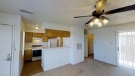 This efficiency unit offers a well-designed, single-floor layout that maximizes every square foot. The open-concept living and kitchen area creates a seamless flow throughout the space, making it feel bright and practical. The kitchen is equipped with an electric range, refrigerator, and a built-in ventilation hood, all complemented by warm wood-toned cabinetry and a peninsula-style breakfast bar that doubles as a workspace or dining area. A textured ceiling adds character overhead, while a ceiling fan with an integrated light fixture provides both comfort and illumination to the main living area. The flooring transitions between wood-look and tile surfaces, adding visual interest throughout. A wall-mounted HVAC panel provides convenient climate control. Toward the rear of the unit, a spacious walk-in closet offers generous storage, and a separate utility or bathroom area is accessible through a hallway. The overall ambiance is clean, neutral, and move-in ready, making this efficiency an ideal space for those seeking a functional and low-maintenance living environment.