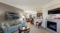 This single-story residence offers a thoughtfully designed open-concept layout that connects the living, dining, and kitchen areas into one cohesive, airy space. The living room features plush carpeting, crown molding, a fireplace, and sliding glass doors that invite natural light and provide direct access to a private patio with outdoor views. A dedicated dining area sits adjacent to the living space, highlighted by a contemporary chandelier and crown molding detail.

The galley-style kitchen is well-equipped with rich dark cabinetry, granite countertops, and black appliances including a range, microwave, refrigerator, and dishwasher. A peninsula with bar seating bridges the kitchen to the living area. A dedicated in-unit laundry room is conveniently accessible directly from the kitchen.

The residence includes two bedrooms, each with generous closet space and soft carpeting. The primary bedroom features large windows for ample natural light. The bathroom offers dark vanity cabinetry, neutral tile flooring, and a tiled shower, maintaining a clean, cohesive aesthetic throughout the home.