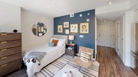 Located at 33 N St NE in Washington, DC, this thoughtfully designed studio offers a seamless open-concept layout that integrates the living, sleeping, and kitchen areas into one cohesive space. The living and sleeping area is anchored by a striking deep-blue accent wall adorned with framed artwork, complemented by warm hardwood flooring and a bright, airy atmosphere. Floor-to-ceiling windows with sleek black frames flood the space with natural light and open to a private outdoor terrace overlooking lush greenery and the surrounding cityscape — a standout feature of this unit. The modern kitchen is well-appointed with two-tone cabinetry featuring white upper cabinets and rich walnut lower drawers, a neutral quartz countertop, a glossy tile backsplash, and a full suite of stainless steel appliances including a range, built-in microwave, dishwasher, and refrigerator. The bathroom continues the contemporary aesthetic with large-format dark tile flooring, gray walls, a glass-enclosed shower with tiled surround, and a floating walnut vanity topped with a crisp white countertop. Every detail of this space reflects a clean, modern design sensibility suited for urban living in the heart of Washington, DC.