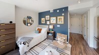 Located at 33 N St NE in Washington, DC, this thoughtfully designed studio offers a seamless open-concept layout that integrates the living, sleeping, and kitchen areas into one cohesive space. The living and sleeping area is anchored by a striking deep-blue accent wall adorned with framed artwork, complemented by warm hardwood flooring and a bright, airy atmosphere. Floor-to-ceiling windows with sleek black frames flood the space with natural light and open to a private outdoor terrace overlooking lush greenery and the surrounding cityscape — a standout feature of this unit. The modern kitchen is well-appointed with two-tone cabinetry featuring white upper cabinets and rich walnut lower drawers, a neutral quartz countertop, a glossy tile backsplash, and a full suite of stainless steel appliances including a range, built-in microwave, dishwasher, and refrigerator. The bathroom continues the contemporary aesthetic with large-format dark tile flooring, gray walls, a glass-enclosed shower with tiled surround, and a floating walnut vanity topped with a crisp white countertop. Every detail of this space reflects a clean, modern design sensibility suited for urban living in the heart of Washington, DC.
