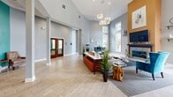 This leasing center in Memphis, Tennessee offers a polished and inviting environment designed to impress visitors from the moment they arrive. The single-floor space is characterized by dramatically soaring vaulted ceilings that lend an expansive, airy atmosphere throughout. Light wood-look tile flooring laid in a classic herringbone pattern anchors the interior with a refined yet approachable aesthetic.

Large windows positioned at varying heights flood the space with natural light, providing views of the surrounding outdoor environment and reinforcing the open, welcoming feel. The main area is thoughtfully arranged with distinct zones, including a comfortable lounge seating area centered around a sleek fireplace with a warm amber accent wall, creating an inviting focal point. Stylish pendant lighting fixtures hang above, adding warmth and visual interest to the space.

A long reception counter serves as the leasing hub, accompanied by tufted orange bench seating that introduces a vibrant pop of color. Teal accent chairs and lush indoor plants are strategically placed throughout, contributing to a lively yet sophisticated palette. A charming vintage-style popcorn cart adds a playful, memorable touch near the entrance. Structural columns define areas without obstructing sightlines, while rich wood-toned double doors provide access to additional private spaces. The overall ambiance is modern, bright, and professionally curated.