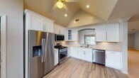 Located within the Fairfield Knolls South community at Pineview Lane in Coram, New York, this two-floor home offers a well-appointed layout across thoughtfully designed living spaces. The kitchen is a standout feature, boasting soaring vaulted ceilings, crisp white shaker cabinetry, a marble-style tile backsplash, light wood-look flooring, and a full suite of stainless steel appliances including a gas range, built-in microwave, dishwasher, and a French door refrigerator. An arched pass-through adds an elegant architectural touch, while a window above the sink invites natural light. The expansive main living area features elevated ceilings with crown molding, a ceiling fan with recessed lighting, and soft carpeting throughout, creating a comfortable and open atmosphere. Bedrooms are generously proportioned with plush carpet, ceiling fans, large windows overlooking greenery, and access to walk-in closets. Bathrooms are clean and functional, with one offering a glass-enclosed tub-shower combo with tile surround and another featuring a walk-in glass shower with a dark granite vanity. An attached single-car garage with an automatic opener provides convenient enclosed parking and additional storage. Six-panel interior doors with brass hardware are found throughout the home, adding a consistent, classic design detail.