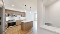 Located at 2525 Via Alta in San Diego's Mission Valley area, this well-appointed one-bedroom, one-bathroom residence offers a thoughtfully designed open-concept layout. Light hardwood flooring flows throughout the main living areas, creating a warm and cohesive aesthetic.

The kitchen is a standout feature, showcasing flat-panel warm wood cabinetry, a crisp white subway tile backsplash, and a substantial central island topped with quartz countertops. Elegant pendant lighting hangs above the island, while stainless steel appliances — including a gas range, built-in microwave, dishwasher, and French door refrigerator — complete the space. The kitchen opens seamlessly into the living area, enhancing the sense of openness and flow.

The spacious bedroom is finished with plush carpeting and features a large sliding glass door that opens to a private balcony with scenic outdoor views, allowing ample natural light to fill the room. A dedicated closet provides generous storage.

The bathroom is clean and modern, featuring light wood-tone cabinetry, a combination tub and shower, and hardwood-style flooring. A walk-in closet is conveniently accessible directly from the bathroom. The hallway connects all areas efficiently, contributing to the unit's smart, functional design. Overall, the space exudes a contemporary, move-in-ready feel with high-quality finishes throughout.