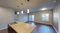 This single-story, 3-bedroom, 2-bathroom home in Conroe, TX offers a well-designed open-concept layout that seamlessly connects the kitchen, dining, and living areas. The kitchen is a standout feature, showcasing rich dark cabinetry, granite countertops, a mosaic tile backsplash, black appliances including a refrigerator, range, and built-in microwave, and a large center island with a sink and pendant lighting overhead. Wood-look flooring flows throughout the main living areas, adding warmth and durability. The living room is bright and inviting, with a ceiling fan, French doors leading to the outdoors, and additional windows that allow natural light to fill the space. Each of the three bedrooms is carpeted for comfort and equipped with a ceiling fan, with windows providing outdoor views. The bedrooms include closet storage, with at least one featuring a sliding-door closet. Both bathrooms are finished with granite-topped dark vanities, wood-look flooring, and tiled tub/shower combinations. The neutral color palette and consistent finishes throughout give the home a cohesive, modern aesthetic well-suited for comfortable everyday living.