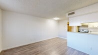 This single-floor unit offers a clean, functional layout designed for comfortable everyday living. The open-concept living area is finished with warm wood-look laminate flooring that runs continuously throughout the space, creating a cohesive and easy-to-maintain environment. Neutral white walls and a textured popcorn ceiling contribute to a bright, understated aesthetic.

The kitchen is positioned along one side of the living area, featuring a peninsula with a light-toned stone countertop that doubles as a breakfast bar. White cabinetry provides ample storage, while stainless steel appliances, including a refrigerator and range, add a modern touch. A stainless steel sink is conveniently integrated into the peninsula counter.

Adjacent to the kitchen, a dedicated utility area houses in-unit washer and dryer connections, complemented by built-in shelving for additional storage. White cabinetry with stone countertops continues in this space, maintaining a consistent design language throughout.

The bedroom is a generously proportioned room with the same wood-look flooring, a textured ceiling, and a window that admits natural light. A mirrored sliding-door closet provides practical storage while visually expanding the room. Overall, the unit presents a well-organized, move-in-ready space with a clean and neutral palette.