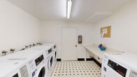 Located at 801 D St in Davis, California, this shared laundry facility offers a clean, well-organized space designed for practical, everyday use. The room is finished with a classic black-and-white diamond-patterned tile floor and bright white walls, creating a tidy and functional environment. Overhead fluorescent lighting ensures the space is well-lit throughout.

Multiple front-loading washing machines and top-loading dryers are arranged along the walls, providing ample capacity for users. The machines are modern and clearly labeled, with accessible units marked for those with mobility needs. A built-in folding counter along one wall offers a convenient surface for sorting and folding laundry, accompanied by a corkboard for posting notices and information.

A utility sink area is tucked into a corner of the room, complete with wall-mounted faucets and a trash receptacle, adding to the overall utility of the space. A fire extinguisher is mounted near the entry door, reflecting attention to safety. Ventilation is provided through a wall vent, keeping the space comfortable during use. The single-level layout and accessible design make this laundry facility a straightforward, efficiently arranged shared amenity.