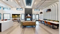 Located at 2300 N Broad St in Fuquay-Varina, NC, this contemporary single-floor amenity space offers a thoughtfully designed environment ideal for gathering and recreation. The open-concept living and lounge area serves as the centerpiece, boasting soaring ceilings with a striking coffered detail, recessed lighting, and large clerestory windows that flood the space with natural light. A dramatic floor-to-ceiling fireplace, clad in bold geometric black-and-white tile with a wood mantle, anchors the room alongside a wall-mounted TV. Wide-format tile flooring and a geometric patterned accent area near the entrance add visual depth throughout.

The kitchen features sleek grey cabinetry, quartz countertops, a stainless steel sink with a pro-style faucet, under-counter refrigeration units, and a stone tile backsplash — all complemented by dual wall-mounted screens above. The dining area is defined by dramatic arc pendant lighting and a long communal table with cognac leather chairs, while a separate dining room provides a quieter setting with a wood table, upholstered seating, and a large window overlooking lush outdoor greenery.

A dedicated game room houses a full-size billiards table beneath soaring windows and a geometric chandelier, with a shuffleboard table nearby. The connecting hallway links each zone seamlessly, completing this well-appointed, multifunctional space.