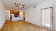 This studio in Leander, TX offers a thoughtfully designed single-floor open-concept layout that efficiently combines the living and kitchen areas into one cohesive space. Light wood-style flooring runs throughout, creating a bright, clean aesthetic complemented by crisp white walls and recessed lighting. A ceiling fan in the main living area adds both comfort and style.

The kitchen is a standout feature, equipped with warm-toned wood cabinetry, stainless steel appliances including a refrigerator with ice dispenser, a range, and a microwave. A granite-topped peninsula with an undermount sink serves as a natural divider between the kitchen and living area, offering additional prep and seating space. A tiled backsplash adds a polished finishing touch.

The studio includes two bathrooms, one of which features a full tub-shower combination with white tile surround, a wood-toned vanity with granite countertop, and wood-look tile flooring. A dedicated closet provides practical storage. Natural light enters through a windowed entry door and additional windows, keeping the space feeling open and airy. In-unit stacked laundry is also present, adding everyday convenience to this efficiently designed studio.