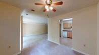 This single-floor residence offers a practical and comfortable layout designed to maximize usable space throughout. The living area is open and generously sized, finished with neutral-toned carpet and warm cream-painted walls. A ceiling fan with an integrated light fixture anchors the room, providing both air circulation and ambient lighting. Large sliding glass doors with vertical blinds open to a balcony overlooking lush greenery, bringing in natural light and pleasant outdoor views.

The kitchen is efficiently arranged in an L-shaped configuration, featuring warm honey-toned cabinetry with ample upper and lower storage, dark laminate countertops, and white appliances including a gas range, dishwasher, and refrigerator. A utility light overhead brightens the workspace effectively.

The bedrooms are carpeted and well-proportioned, maintaining the same neutral color scheme found throughout the unit. One bedroom features a walk-in closet outfitted with built-in shelving and hanging rods on multiple walls, offering substantial storage capacity. Additional windows dressed with vertical blinds allow natural light to filter into the sleeping areas.

The bathroom is cleanly finished with a single-sink vanity featuring warm wood cabinetry, a mirrored medicine cabinet, and a full tub-shower combination with white tile surround. The overall ambiance of the space is practical, clean, and move-in ready.
