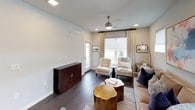 This single-floor residence showcases a thoughtfully designed interior that balances modern aesthetics with comfortable living. The living area is highlighted by dark hardwood flooring, a ceiling fan, and multiple windows dressed with roller shades and patterned drapes, allowing ample natural light to fill the space. A neutral color palette is complemented by curated furnishings, including tufted accent chairs, a plush sofa adorned with navy and geometric-patterned pillows, and gold-toned accent tables. A bold abstract artwork serves as a focal point above the sofa, adding a vibrant touch.

The kitchen features a galley-style layout with two-tone cabinetry — crisp white uppers paired with wood-grain lowers — white quartz countertops, a tile backsplash, and a full suite of stainless steel appliances. Pendant lighting with metallic dome shades adds a contemporary accent.

The bedrooms are carpeted and feature tray ceilings with ceiling fans, large windows with outdoor views, and generous proportions. The bathroom is finished with a floating white vanity, backlit mirror, dark hardwood-style flooring, and a frameless sliding glass shower enclosure, conveying a clean, spa-like atmosphere throughout.