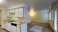 This single-floor residence offers a practical and well-organized layout designed for comfortable everyday living. The kitchen is outfitted with white cabinetry that provides ample storage space, light-toned countertops, and a built-in sink and dishwasher, making it fully equipped for daily use. A half-wall partition separates the kitchen from the adjacent living area, creating a sense of definition between the two spaces while maintaining an open and connected feel throughout. The living area features wall-to-wall carpeting that adds warmth and comfort underfoot, with neutral-toned walls that lend a clean and versatile backdrop suitable for a variety of interior styles. The open flow between the kitchen and living space makes the layout feel spacious and functional. The overall design of the residence emphasizes simplicity and practicality, with consistent neutral tones used throughout to create a cohesive and calm atmosphere. The single-floor layout ensures easy accessibility and a straightforward floor plan that is intuitive to navigate. This space presents a tidy, move-in-ready environment well-suited for those seeking a low-maintenance yet comfortable place to call home.