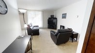 This single-floor unit is thoughtfully arranged across a well-proportioned footprint, as seen in the 3D floor plan. The layout includes a generously sized living area, a separate bedroom, a kitchen, and at least one bathroom, providing a functional and organized flow throughout the space.

The living room serves as the heart of the unit, featuring wall-to-wall carpeting that adds warmth underfoot. A large window dressed with vertical blinds allows abundant natural light to fill the room, creating a bright and open atmosphere. The space comfortably accommodates a full seating arrangement, including a sofa and reclining chair, with ample room remaining for additional furnishings.

The kitchen area is positioned adjacent to the living space and appears to offer standard cabinetry and countertop workspace. The bedroom, visible in the floor plan, is a well-sized room capable of accommodating a full bed frame and additional furniture.

The overall layout promotes easy navigation between rooms, with a centrally located entry point connecting the key living zones. The predominantly neutral color palette throughout — white walls, light ceilings, and beige carpeting — creates a clean, cohesive aesthetic that is both versatile and welcoming.