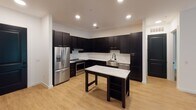 Located on Barclay Downs Drive in Charlotte, NC, this single-floor unit showcases a contemporary design defined by a cohesive dark and light color palette throughout. The kitchen is a standout feature, outfitted with floor-to-ceiling dark espresso cabinetry, marble-look quartz countertops, a white subway tile backsplash, and a full suite of stainless steel appliances including a French door refrigerator and slide-in range. A freestanding island with matching marble-look surface provides additional prep and dining space. Light wood-tone flooring flows throughout the open living areas, complemented by recessed lighting and modern ceiling fans. The living area is bright and open, with natural light streaming in through large windows and direct access to an outdoor balcony. Distinctive black barn doors add a stylish architectural accent. The bedrooms are well-proportioned, each featuring ceiling fans, large windows with outdoor views, and access to closet space. The primary bathroom is generously sized with a dual-sink vanity featuring dark cabinetry with gold hardware, marble-look countertops, a soaking tub, a glass-enclosed shower, light tile flooring, and a walk-in closet. A secondary bathroom mirrors the refined aesthetic with similar finishes and its own walk-in closet access.