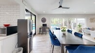 Located at 2800 S Mission Rd in Tucson, AZ, this well-appointed single-floor space offers a clean, modern design with a cohesive open layout. Light wood-look tile flooring flows throughout, tying together the living, dining, and kitchen areas with a bright, airy aesthetic.

The combined living and dining room serves as the heart of the space. The living area features a comfortable sofa, a wall-mounted flat-screen TV, a round wood coffee table, and a ceiling fan for year-round comfort. Large sliding glass doors span nearly the full width of one wall, flooding the room with natural light and offering direct views of an outdoor pool and patio area. The dining area includes a dark wood table surrounded by bold blue velvet chairs, a ceiling fan overhead, and a dedicated workstation tucked neatly against the wall. Additional french doors provide a second point of access to the outdoor pool deck.

A cozy seating nook with two blue accent chairs and a whiteboard wall offers a quiet retreat or collaborative space. The kitchen is crisp and functional, featuring white shaker cabinetry, white subway tile backsplash, light countertops, and stainless steel appliances including a full-size refrigerator and microwave. A window above the counter brings in additional natural light. Recessed lighting throughout ensures the entire space remains bright and welcoming.