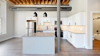 Located at 251 N Rose St in downtown Kalamazoo, MI, this 2-bedroom, 2-bathroom loft-style residence blends industrial character with modern finishes. The open-concept living, dining, and kitchen area serves as the heart of the home, anchored by an exposed wood beam ceiling, visible ductwork, and a structural steel column that nod to the building's heritage. The kitchen is well-appointed with white shaker cabinetry, granite countertops, a subway tile backsplash, stainless steel appliances including a full-size refrigerator and dishwasher, and a central island with pendant lighting above.

Both bedrooms feature wood-look flooring, exposed beam ceilings, and large windows that invite generous natural light and views of the surrounding urban streetscape. Each bedroom includes closet space, with clean-lined panel doors and matte black hardware consistent throughout the unit.

The two bathrooms are finished with textured tile surrounds and matte black fixtures. One bathroom features a soaking tub-shower combination, while the second offers a walk-in shower with built-in shelving. A dedicated laundry room and multiple closets add practical functionality. Light-toned walls and wood-look flooring create a cohesive, contemporary feel throughout the entire residence.