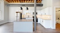 Located at 251 N Rose St in downtown Kalamazoo, MI, this 2-bedroom, 2-bathroom loft-style residence blends industrial character with modern finishes. The open-concept living, dining, and kitchen area serves as the heart of the home, anchored by an exposed wood beam ceiling, visible ductwork, and a structural steel column that nod to the building's heritage. The kitchen is well-appointed with white shaker cabinetry, granite countertops, a subway tile backsplash, stainless steel appliances including a full-size refrigerator and dishwasher, and a central island with pendant lighting above.

Both bedrooms feature wood-look flooring, exposed beam ceilings, and large windows that invite generous natural light and views of the surrounding urban streetscape. Each bedroom includes closet space, with clean-lined panel doors and matte black hardware consistent throughout the unit.

The two bathrooms are finished with textured tile surrounds and matte black fixtures. One bathroom features a soaking tub-shower combination, while the second offers a walk-in shower with built-in shelving. A dedicated laundry room and multiple closets add practical functionality. Light-toned walls and wood-look flooring create a cohesive, contemporary feel throughout the entire residence.