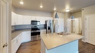 This single-floor residence offers a thoughtfully designed layout with a clean, contemporary aesthetic throughout. The open-concept kitchen serves as a central hub, showcasing white shaker-style cabinetry, stainless steel appliances including a French door refrigerator, electric range, and built-in microwave. A large island with a double stainless steel sink and pendant lighting overhead adds both functionality and style. Wood-look plank flooring runs throughout the main living areas, complementing the neutral warm-gray color palette on the walls.

The spacious living area flows naturally from the kitchen, offering an open and airy feel with easy access to additional rooms via a private entry door with sidelight glass panels. Bedrooms are finished with plush carpet and feature windows with blinds that invite natural light.

Two bathrooms serve the unit, each designed with white cabinetry, stone-look countertops, large vanity mirrors, and wood-look or tile flooring. The full bathroom includes a walk-in shower area and additional wall-mounted storage cabinetry, while the secondary bathroom provides a clean and efficient layout. Recessed lighting and flush-mount fixtures illuminate the space throughout, contributing to a bright and welcoming atmosphere.