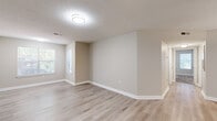 This single-floor residence offers a thoughtfully designed layout with a cohesive neutral color palette and consistent finishes throughout. The open-concept living and dining area is anchored by light hardwood-style flooring, a textured ceiling, and a window that brings in natural light, creating a bright and welcoming atmosphere. The space flows seamlessly into the kitchen, which is a standout feature of the unit. It is equipped with stainless steel appliances — including a refrigerator, electric range, built-in microwave, and dishwasher — complemented by crisp white cabinetry, light granite-style countertops, and a stylish mosaic tile backsplash. A peninsula counter with a pendant light above defines the kitchen's connection to the living area. The bedrooms are carpeted for comfort and benefit from multiple windows that allow ample natural light to fill each room. A hallway connects the private areas of the residence, where a bathroom features a white vanity with under-cabinet storage and a mirrored medicine cabinet. Closet space is available adjacent to the bathroom, with wire shelving for practical organization. Throughout, white trim and baseboards provide clean contrast against the warm beige walls, lending the space a polished, move-in-ready appearance.