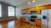 Located at 89 Globe Mills Ave in Fall River, Massachusetts, this single-floor residence offers a thoughtfully designed living space with a blend of classic character and modern finishes throughout. Rich hardwood flooring flows continuously across the main living areas, reflecting natural light and adding warmth to every room.

The open kitchen is a functional highlight, equipped with a full suite of stainless steel appliances — including a refrigerator with ice maker, electric range, built-in microwave, and dishwasher. Warm honey-toned wood cabinetry lines the walls, complemented by granite countertops that provide ample prep space. Tall arched windows flood the kitchen and adjacent living area with natural light, enhancing the airy feel.

The living area impresses with soaring ceilings and a ceiling fan, creating a spacious and comfortable atmosphere. Structural columns add an architectural character reminiscent of the building's historic mill origins. The bedroom features generous closet space and direct access to adjoining rooms, maintaining a practical and connected layout.

The bathroom is finished with tile flooring, a granite-topped vanity with wood cabinetry, and a full tub-shower combination. Neutral wall tones throughout the unit create a cohesive and versatile aesthetic, ready to accommodate a variety of décor styles.