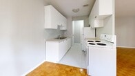 This thoughtfully designed 1-bedroom, 1-bathroom unit spans a single floor and offers a functional, efficient layout throughout. Warm parquet flooring flows consistently through the living areas and bedroom, lending a classic character to the space.

The combined kitchen and living room area anchors the unit. The kitchen is configured in a galley style, featuring white cabinetry on both sides, a four-burner coil electric range, a refrigerator, a stainless steel sink, and light countertops — all finished in a clean, all-white palette. The living area is open and bright, with large sliding glass doors that lead directly to a private balcony, offering outdoor views and generous natural light.

The bedroom is a comfortable size, featuring a window with an outdoor view, a baseboard heating unit, and a built-in closet with a sliding door and hanging rod. The adjoining hallway provides access between rooms and connects the bedroom to the rest of the unit.

The bathroom is finished with white tile and includes a bathtub with a handheld showerhead. Throughout the unit, neutral grey walls, white trim, and consistent flooring create a cohesive, understated aesthetic that is easy to personalize.