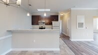 Located at 925 Seasons Dr in Gastonia, NC, this single-floor residence offers a thoughtfully designed layout with a cohesive, neutral aesthetic throughout. The open-concept kitchen serves as a central hub, featuring rich dark-espresso cabinetry, granite-style countertops, stainless steel appliances including a built-in microwave and electric range, and a peninsula that provides both workspace and a natural divide between the kitchen and adjoining living areas. Pendant lighting above the peninsula adds a warm, finishing touch. Tile flooring flows through the kitchen and into what appears to be a dedicated dining area, which is accented by chair-rail molding and an elegant chandelier.

The living and bedroom areas feature light gray luxury vinyl plank flooring, complemented by warm beige walls and crisp white trim and crown molding. Large windows fitted with horizontal blinds allow abundant natural light while offering views of the surrounding community. A sliding glass door opens to an outdoor balcony. The bathroom is finished with matching dark cabinetry, granite countertops, and tile flooring, and includes a built-in shelving nook. A dedicated laundry space with washer and dryer connections completes the practical interior layout.