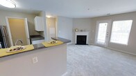 This single-floor space offers an open-concept design that seamlessly connects the kitchen and living area, creating a cohesive and functional layout. The kitchen features dark granite-style countertops, white cabinetry, and a peninsula with bar seating — an ideal spot for casual dining or meal prep. The countertops provide ample workspace, and the layout allows for easy interaction between the kitchen and the main living area.

The living room is finished with plush, neutral-toned carpeting that adds warmth underfoot. A classic white-framed fireplace serves as the room's focal point, complete with a mantel that offers space for décor. The fireplace adds both visual interest and a sense of comfort to the space.

Natural light flows in through a glass patio door along the far wall, brightening the room and providing outdoor access. The walls are painted in soft, warm neutral tones throughout, contributing to the space's calm and welcoming ambiance. The open layout and consistent finishes give the space a clean, well-connected feel from kitchen to living area.