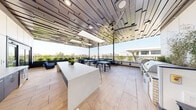 Located at 357 E 500 S in Salt Lake City, Utah, this rooftop amenity deck offers a sophisticated open-air gathering space with a seamless blend of indoor comfort and outdoor living. The space is anchored by a striking architectural pergola ceiling composed of layered, offset wood-tone slats, lending a dynamic geometric aesthetic overhead while large ceiling fans provide airflow throughout.

Light-toned large-format tile flooring extends across the entire deck, creating a clean, contemporary foundation. A central white island counter serves as the focal point of the interior-facing zone, flanked by bar-height seating and planter accents. An outdoor kitchen station along one wall is equipped with professional-grade grills and ample prep surfaces, making the space well-suited for entertaining.

Multiple dining tables with modern blue, white, and dark metal chairs are arranged throughout, accommodating a variety of group sizes. A dedicated lounge area along the open-air perimeter features plush sofas, accent stools, and lush greenery in raised planters, providing a relaxed retreat.

The open railings along the terrace edges frame sweeping panoramic views of the Salt Lake City skyline and the Wasatch Mountain Range beyond, filling the space with abundant natural light and creating a vibrant, inviting atmosphere ideal for social gatherings and relaxation.