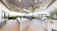Located at 357 E 500 S in Salt Lake City, Utah, this rooftop amenity deck offers a sophisticated open-air gathering space with a seamless blend of indoor comfort and outdoor living. The space is anchored by a striking architectural pergola ceiling composed of layered, offset wood-tone slats, lending a dynamic geometric aesthetic overhead while large ceiling fans provide airflow throughout.

Light-toned large-format tile flooring extends across the entire deck, creating a clean, contemporary foundation. A central white island counter serves as the focal point of the interior-facing zone, flanked by bar-height seating and planter accents. An outdoor kitchen station along one wall is equipped with professional-grade grills and ample prep surfaces, making the space well-suited for entertaining.

Multiple dining tables with modern blue, white, and dark metal chairs are arranged throughout, accommodating a variety of group sizes. A dedicated lounge area along the open-air perimeter features plush sofas, accent stools, and lush greenery in raised planters, providing a relaxed retreat.

The open railings along the terrace edges frame sweeping panoramic views of the Salt Lake City skyline and the Wasatch Mountain Range beyond, filling the space with abundant natural light and creating a vibrant, inviting atmosphere ideal for social gatherings and relaxation.