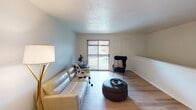 This single-floor residence offers a thoughtfully laid-out living space with a clean, contemporary aesthetic throughout. The living room is an inviting and open area finished with light hardwood-style flooring, soft blue-toned walls, and a sliding glass door that opens to a private balcony, filling the room with natural light and providing an outdoor view. The space accommodates comfortable seating and a relaxed, functional arrangement.

The galley-style kitchen is efficiently designed with white shaker cabinetry, light countertops, and stainless steel and black appliances, including a range and refrigerator. A stainless steel sink sits opposite the range, making the kitchen both practical and easy to navigate. Adjacent to the kitchen, a dedicated dining area provides space for a round table and seating, conveniently positioned for everyday use.

The bedroom is a quiet, carpeted retreat with neutral walls, a closet with built-in rod storage, and easy access to the rest of the unit. The room comfortably fits a full-sized bed and additional furniture such as a dresser. The full bathroom features a white vanity with under-cabinet storage, overhead lighting, open wall shelving, and a shower-tub combination, all finished with light hardwood-style flooring for a clean, cohesive look.