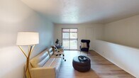 This single-floor residence offers a thoughtfully laid-out living space with a clean, contemporary aesthetic throughout. The living room is an inviting and open area finished with light hardwood-style flooring, soft blue-toned walls, and a sliding glass door that opens to a private balcony, filling the room with natural light and providing an outdoor view. The space accommodates comfortable seating and a relaxed, functional arrangement.

The galley-style kitchen is efficiently designed with white shaker cabinetry, light countertops, and stainless steel and black appliances, including a range and refrigerator. A stainless steel sink sits opposite the range, making the kitchen both practical and easy to navigate. Adjacent to the kitchen, a dedicated dining area provides space for a round table and seating, conveniently positioned for everyday use.

The bedroom is a quiet, carpeted retreat with neutral walls, a closet with built-in rod storage, and easy access to the rest of the unit. The room comfortably fits a full-sized bed and additional furniture such as a dresser. The full bathroom features a white vanity with under-cabinet storage, overhead lighting, open wall shelving, and a shower-tub combination, all finished with light hardwood-style flooring for a clean, cohesive look.