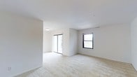 Located at 41 Emily Drive in South Setauket, New York, this single-floor residence offers a clean, modern layout designed for comfortable living. The interior is characterized by bright white walls and smooth ceilings that contribute to an airy, open atmosphere throughout the space.

The living area is generously proportioned, featuring wall-to-wall plush carpeting in a neutral tone that adds warmth underfoot and complements the light color palette. A sliding glass door provides direct access to the outdoors while flooding the room with an abundance of natural light, creating a seamless indoor-outdoor connection. An additional double-hung window on the adjacent wall further enhances the bright and welcoming ambiance, offering views of the surrounding greenery.

The open layout allows for flexible furniture arrangements, making the space highly functional and adaptable. Ceiling-mounted lighting provides consistent illumination throughout, and the recessed ceiling design adds a subtle architectural detail. The overall design aesthetic is understated and contemporary, with a neutral palette that serves as an ideal canvas for personalization. The combination of natural light, open space, and quality finishes makes this residence a comfortable and inviting place to call home.
