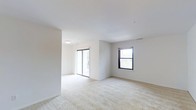 Located at 41 Emily Drive in South Setauket, New York, this single-floor residence offers a clean, modern layout designed for comfortable living. The interior is characterized by bright white walls and smooth ceilings that contribute to an airy, open atmosphere throughout the space.

The living area is generously proportioned, featuring wall-to-wall plush carpeting in a neutral tone that adds warmth underfoot and complements the light color palette. A sliding glass door provides direct access to the outdoors while flooding the room with an abundance of natural light, creating a seamless indoor-outdoor connection. An additional double-hung window on the adjacent wall further enhances the bright and welcoming ambiance, offering views of the surrounding greenery.

The open layout allows for flexible furniture arrangements, making the space highly functional and adaptable. Ceiling-mounted lighting provides consistent illumination throughout, and the recessed ceiling design adds a subtle architectural detail. The overall design aesthetic is understated and contemporary, with a neutral palette that serves as an ideal canvas for personalization. The combination of natural light, open space, and quality finishes makes this residence a comfortable and inviting place to call home.