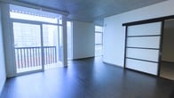 This single-floor space showcases a thoughtfully designed interior that blends industrial and contemporary elements. The exposed concrete ceiling serves as a striking architectural detail, adding raw, urban character throughout the unit. Underfoot, rich dark hardwood flooring contrasts beautifully with the bright white walls, creating a visually balanced aesthetic.

Natural light is a defining feature, with floor-to-ceiling windows wrapping around the living area and offering expansive views of the surrounding cityscape. A glass-paneled sliding door leads to a private balcony, further enhancing the connection between the interior and the urban environment outside.

A standout design element is the black-framed sliding barn door, which adds a modern-industrial touch while offering a space-efficient way to section off areas within the unit. The open-plan layout allows for flexible use of the space, accommodating various furniture arrangements with ease.

Overall, the space delivers a clean, minimalist ambiance with a strong emphasis on natural light, durable materials, and architectural detail — well-suited for urban living with a contemporary sensibility.