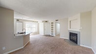 This single-floor residence offers a thoughtfully designed layout that balances comfort and functionality. The open-concept living and dining area is highlighted by plush wall-to-wall carpeting, a textured ceiling, and a tile-surround fireplace that serves as a focal point of the room. Built-in shelving flanks the front entryway, providing convenient storage and display space. Natural light filters in through multiple windows, enhancing the warm, neutral color palette throughout.

The kitchen is equipped with white cabinetry, granite countertops, a subway tile backsplash, and stainless steel appliances including a refrigerator, microwave, and range. A peninsula with an undermount sink adds additional prep and seating space. Track lighting above the kitchen provides focused illumination. Sliding glass doors open directly from the living area onto a private balcony, extending the living space outdoors.

The bedroom is generously sized with soft carpet flooring, neutral walls, and a window that allows natural light to fill the room. An adjoining vanity area with cabinetry leads to the bathroom, which features wood-look vinyl flooring, a tiled tub-shower combination with a decorative accent band, and granite-topped vanity surfaces. The overall design is clean, cohesive, and move-in ready.
