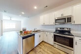 This two-story residence presents a clean, contemporary design with thoughtful finishes throughout both levels. The main floor centers around an open-concept layout where the kitchen flows seamlessly into the living area, creating a bright and connected space. The kitchen is well-equipped, featuring white shaker-style cabinetry with matte black hardware, granite countertops, a classic white subway tile backsplash, and a full suite of stainless steel appliances including a range, microwave, dishwasher, and refrigerator. A peninsula with an undermount sink adds additional prep and storage space. Light wood-style flooring extends throughout the main level, complementing the neutral white walls and recessed lighting overhead.

The staircase, accented by a wood banister and carpeted treads, leads to the upper level, where bedrooms feature plush carpet, ceiling fans, and natural light from well-positioned windows. The upper level also includes a dedicated laundry room with a full-size washer and dryer and shelving for added storage. Bathrooms are finished with white cabinetry, solid-surface countertops, and tile showers, maintaining the home's consistent, modern aesthetic throughout.