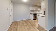 Woodland Trails Unit 303 is a thoughtfully designed one-bedroom, one-bathroom residence situated on a single floor, offering a clean and contemporary living environment throughout. The open-concept layout seamlessly connects the kitchen and living area, creating a versatile and functional space. The kitchen is well-appointed with white shaker-style cabinetry, gray countertops, a stainless steel dishwasher, and a sink with ample workspace, complemented by track lighting overhead. Wood-look luxury vinyl plank flooring flows consistently throughout the unit, lending warmth and visual continuity to every room. The living area is generously proportioned, bathed in natural light from a sliding glass door that opens to the outdoors, providing a welcoming sense of openness. A ceiling light fixture anchors the space. A dedicated in-unit laundry area adds everyday convenience. The bedroom is comfortably sized, featuring a ceiling fan, a window with blinds that invites natural light, and a textured ceiling. The bathroom presents a clean, neutral palette with white cabinetry, a single-basin vanity with gray countertop, a large mirror with above-mirror lighting, and wood-look flooring that ties together the unit's cohesive aesthetic.