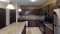 This single-floor residence offers a thoughtfully designed layout with a cohesive, neutral color palette and dark espresso trim throughout. The kitchen serves as a functional centerpiece, showcasing rich dark cabinetry, granite countertops, a central island with pendant lighting, and a full suite of stainless steel appliances including a refrigerator, electric range, microwave, and dishwasher. Tile flooring completes the kitchen's polished look. The living area is generously proportioned, featuring plush carpeting, a window with blinds, and a wall-mounted air conditioning unit, creating a comfortable and versatile space. Multiple bedrooms continue the carpet flooring theme, each equipped with ceiling fans, windows with blinds for natural light control, wall-mounted AC units, and baseboard heating for year-round comfort. The bathrooms are finished with granite-topped dark vanities, undermount sinks, and large mirrors with stylish lighting fixtures. One full bathroom includes a soaking tub, tile flooring, and ample towel storage. Dark-framed interior doors and consistent dark baseboards unify the design throughout, giving the space a clean, modern residential feel.
